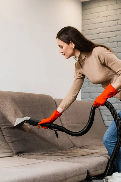 Housekeeper is extracting dirt from upholstered sofa using dry cleaning extractor machine. Cleaner girl is cleaning couch with extraction machine for dry clean upholstered furniture