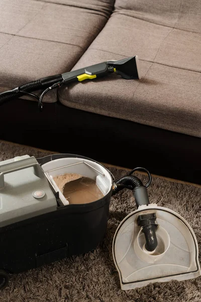 Dry cleaning extractor machine and tank of dirty water after dry cleaning of couch. Professional domestic cleaning service worker is removing dirt and dust from couch using dry cleaning machine
