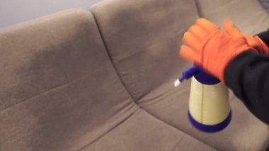 4k video spraying detergent for dry cleaning couch. Professional cleaner girl in gloves is pouring detergent on couch for for removing stains and dirt from couch at home