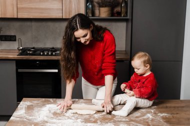 Mother and little helper daughter are preparing cookies and having fun in the kitchen at home. Happy loving family are cooking homemade bakery food together