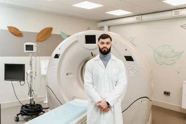 Man doctor in CT scan computed tomography room in medical clinic. Handsome bearded doctor in medical robe with computed tomograph for obtain detailed internal images of the body of patient