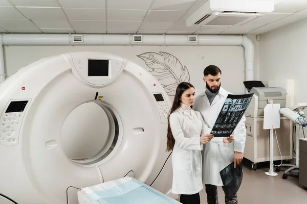 Two doctors discussing x-rays after CT scan of patient abdomen. CT Computed tomography scan procedure to obtain detailed internal images of body and research on tumors in head, brain, and spine