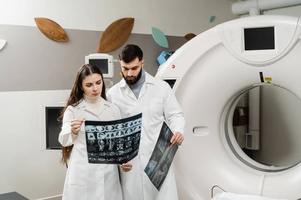 CT Computed tomography scan procedure to obtain detailed internal images of body and research on tumors in head, brain, and spine. Two doctors discussing x-rays after CT scan of patient abdomen