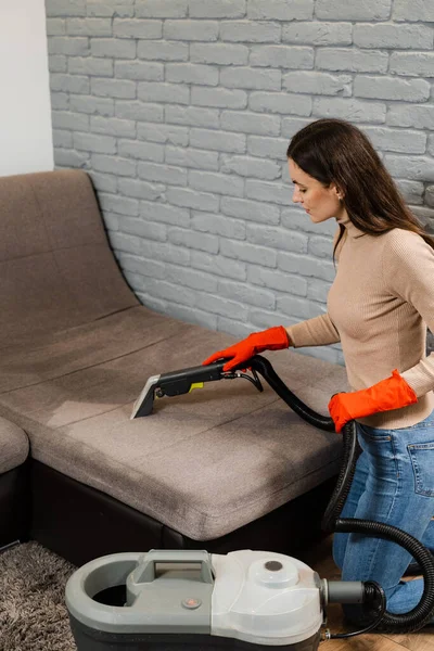 Housekeeper is extracting dirt from upholstered sofa using dry cleaning extractor machine. Cleaner girl is cleaning couch with extraction machine for dry clean upholstered furniture
