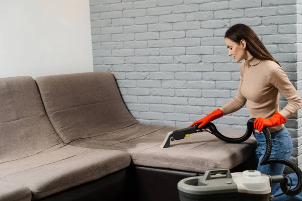 Housewife dry cleaning of upholstered furniture and removing dust, stains and dirt using extractor machine. Cleaner girl is cleaning couch with extractor dry cleaning machine at clients home