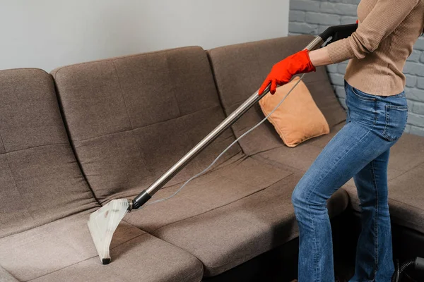 Professional domestic cleaning service worker is removing dirt and dust from couch using dry cleaning machine mop. Dry cleaning extractor mop machine is spraying water and detergent on couch