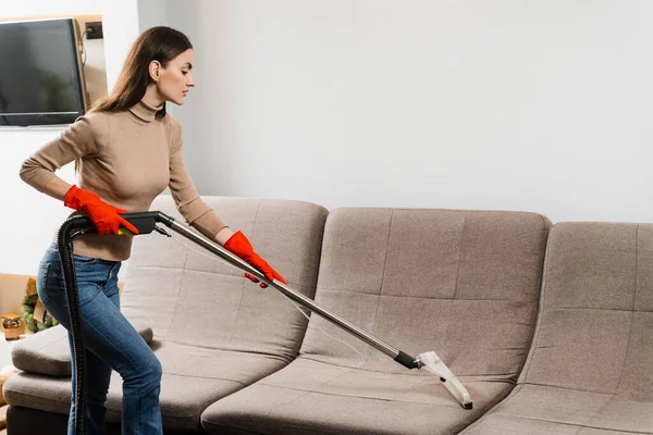 Housewife dry cleaning of couch and removing dust, stains and dirt using mop extractor machine. Cleaner girl is cleaning couch with mop extractor dry cleaning machine at clients home
