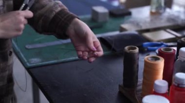 4k video Craftsman is winding and cutting thread for sew genuine leather products. Equipment for genuine leather production in workshop. Process of stitching genuine leather