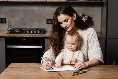 Developing drawing lesson for child toddler at home. Maternity leave. Mom and toddler daughter draw pictures with colored pencils and spend time with mother together