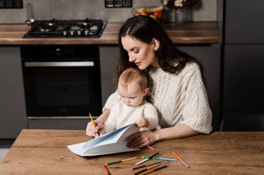 Developing drawing lesson for child toddler at home. Maternity leave. Mom and toddler daughter draw pictures with colored pencils and spend time with mother together