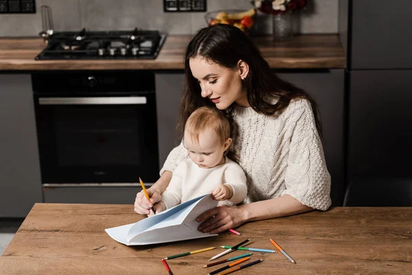 Developing drawing lesson for child toddler at home. Maternity leave. Mom and toddler daughter draw pictures with colored pencils and spend time with mother together