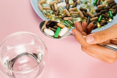 Many dietary supplements tablets, glass of water and spoon for daily pills intake on pink background. Set of mulvitamin, amino acids, minerals and magnesium antistress, melatonin close-up