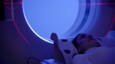 Tıbbi klinikte mavi ışığı olan bir kadının beyin tomografisi. Kız hasta bilgisayarlı tomografi yapıyor. Beyin tümörünün röntgenini çekiyor. Tomografi odasında kırmızı çizgiler var.