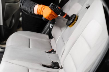 Applying detergent on textile seat in car interior for dry cleaning. Smearing detergent on car textile seats using drill with brush for dry cleaning
