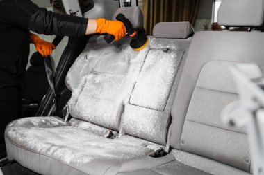 Smearing detergent on car textile seats using drill with brush for dry cleaning. Applying detergent on textile seat in car interior for dry cleaning
