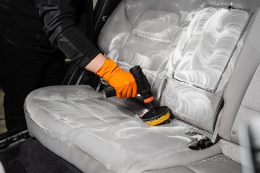 Smearing detergent on car textile seats using drill with brush for dry cleaning. Applying detergent on textile seat in car interior for dry cleaning