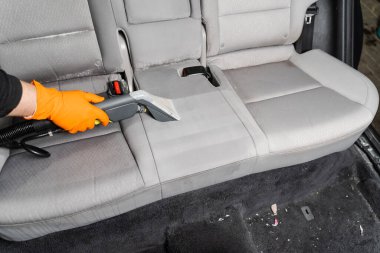 Car cleaner is extracting dirt from car seat using dry cleaning extractor machine. Cleaning textile seats in car interior using extractor machine for dry clean