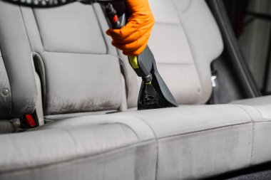 Close-up dry cleaning extractor machine is spraying water and detergent on textile seat inside car. Car dry cleaner is using extraction machine for removing stains and dirt from textile seats