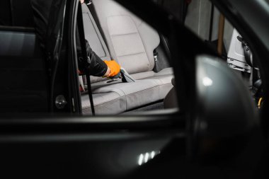 Cleaning textile seats in car interior using extractor machine for dry clean. Car cleaner is extracting dirt from car seat using dry cleaning extractor machine