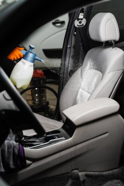 Spraying detergent on textile seats in car interior for dry cleaning. Professional cleaner in gloves is pouring detergent on seat in car for removing stains and dirt