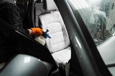Dry wash cleaning for textile seats inside car interior for removing stains and dirt. Spraying detergent on textile seats in car interior for dry cleaning