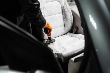 Smearing detergent on car textile seats using drill with brush for dry cleaning. Applying detergent on textile seat in car interior for dry cleaning