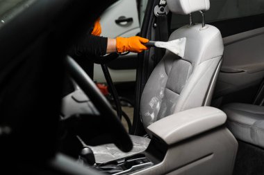 Cleaning textile seats in car interior using extractor machine for dry clean. Car cleaner is extracting dirt from car seat using dry cleaning extractor machine