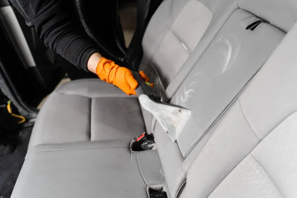 Car cleaner is extracting dirt from car seat using dry cleaning extractor machine. Cleaning textile seats in car interior using extractor machine for dry clean