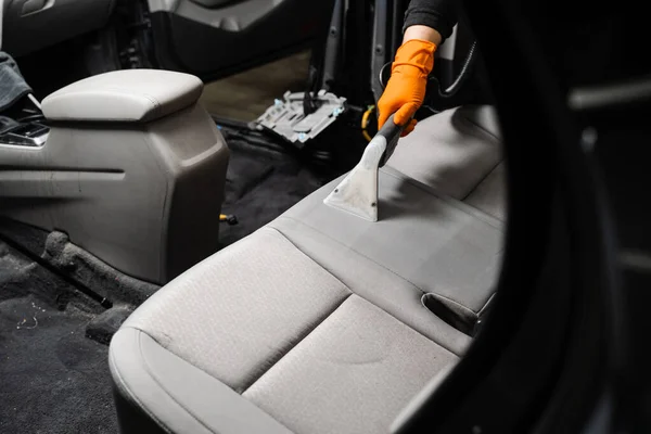 Cleaning textile seats in car interior using extractor machine for dry clean. Car cleaner is extracting dirt from car seat using dry cleaning extractor machine