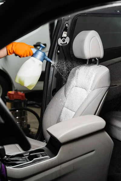 Dry wash cleaning for textile seats inside car interior for removing stains and dirt. Spraying detergent on textile seats in car interior for dry cleaning