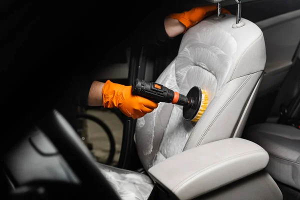 Applying detergent on textile seat in car interior for dry cleaning. Smearing detergent on car textile seats using drill with brush for dry cleaning