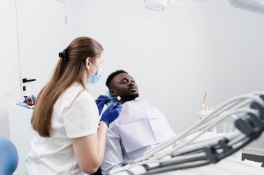 Dişçi, Afrikalı bir adamın dişlerini diş ağrısı tedavisi için inceliyor. Dişlerin ağrıyor. Diş hekimliğinde dişçiye danışmanlık