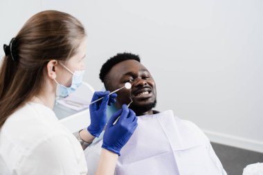 Afro-Amerikan dişçi hastan kutlu olsun. Diş tedavisi. Yakışıklı Afrikalı adam dişçi ofisinde oturuyor ve gülümsüyor. Dişçi muayenesi ve danışma