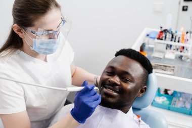Dişçi, Afrikalı bir adamın dişlerini diş ağrısı tedavisi için inceliyor. Dişlerin ağrıyor. Diş hekimliğinde dişçiye danışmanlık
