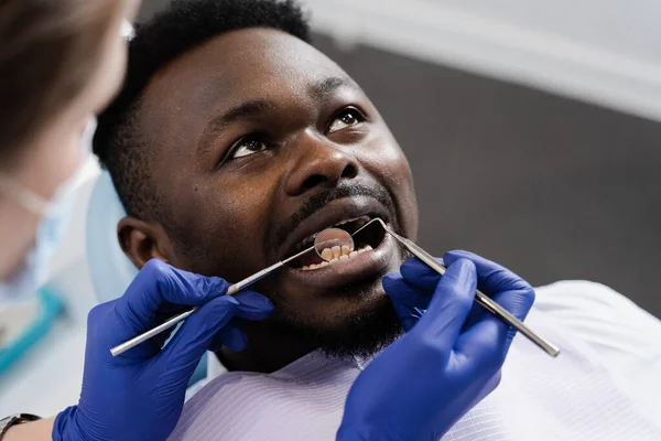 Consultation with dentist at dentistry. Teeth treatment. Dentist examines african man mouth and teeth and treats toothaches. African man patient of dentistry