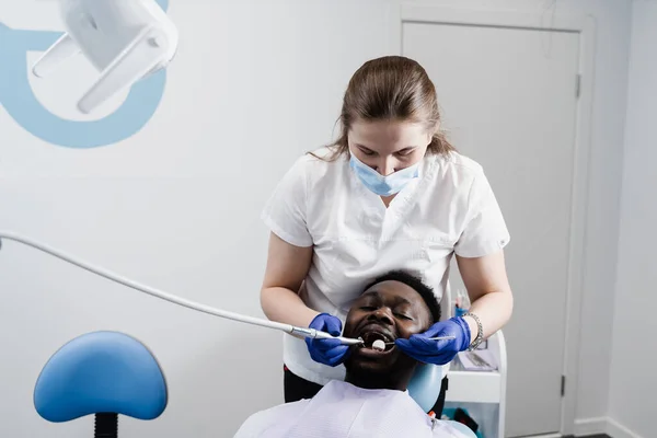 Dentist is drilling teeth and removing caries of african man in dentistry clinic. Teeth treatment. Dental filling for african american man patient