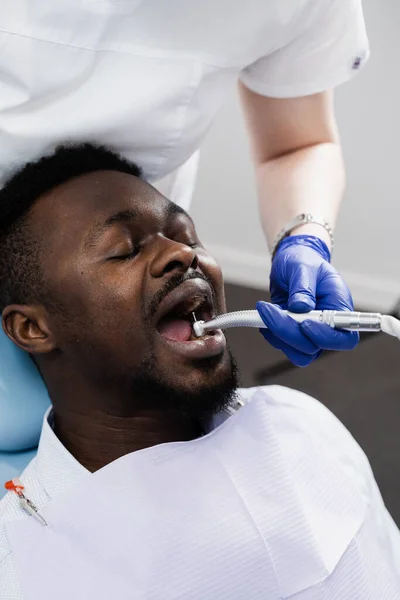 Dental drill for african man in dentistry clinic. Dentist is removing caries and filling teeth for african american patient
