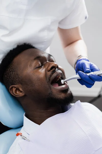 Dental drill for african man in dentistry clinic. Dentist is removing caries and filling teeth for african american patient