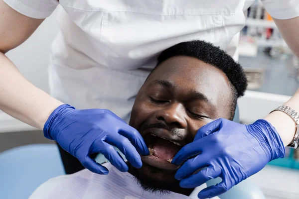 Dentist examines teeth of african man for treatment of toothache. Pain in teeth. Consultation with dentist in dentistry