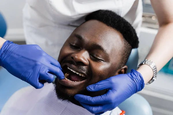 Dentist examines teeth and mouth of african man with blue gloved hands. Dentist touches patient teeth with his hands in dentistry