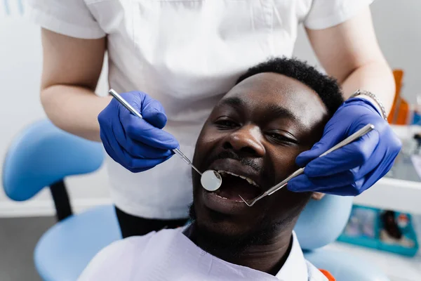 Consultation with dentist at dentistry. Teeth treatment. Dentist examines african man mouth and teeth and treats toothaches. African man patient of dentistry