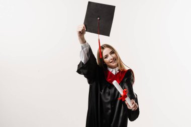 Graduate girl is graduating high school and celebrating academic achievement. Masters degree diploma in hands. Happy student in black graduation gown and cap is smiling on white background