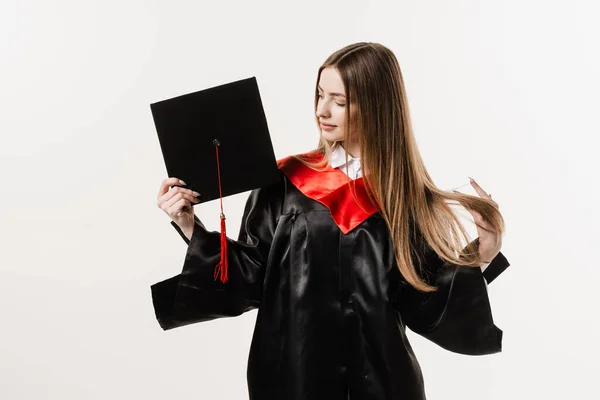 Cheerful bachelor girl in graduation robe and cap on white background. Happy and funny young woman smile. Student achieve master degree in univesity