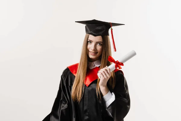 Happy student in black graduation gown and cap is smiling on white background. Graduate girl is graduating high school and celebrating academic achievement. Masters degree diploma in hands