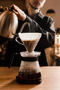 Alternatif filtre kahve demleme metodunu doldur. Barista kavrulmuş ve kağıt filtrede bulunan kahve çekirdeklerinin üzerine sıcak su döküyor.