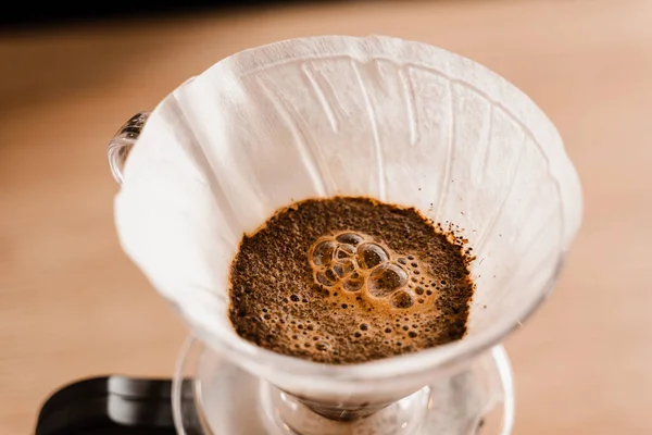 stock image Pour over filter with ground coffee in the funnel in focus. Drip filter coffee brewing. Pour over alternative method of pouring water over roasted and ground coffee beans contained in filter