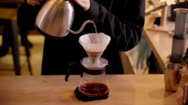 4k video Barista hunide öğütülmüş kahveyle sıcak suyu filtreden döküyor. Damlatma filtresi kahvesi demleniyor. Alternatif su dökme metodunu filtrede bulunan kahve çekirdeklerinin üzerine dökün..