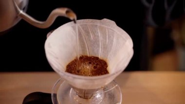 4k video Barista hunide öğütülmüş kahveyle sıcak suyu filtreden döküyor. Damlatma filtresi kahvesi demleniyor. Alternatif su dökme metodunu filtrede bulunan kahve çekirdeklerinin üzerine dökün..