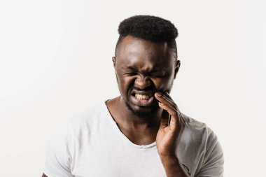 Beyaz arka planda Afrikalı bir adamın diş ağrısı. Afrikalı Amerikalılar yanaklarına dokunuyor ve beyaz arka planda dişlerinin ağrıdığını hissediyorlar. Diş çürüğü, enfeksiyon ya da diş eti yaralanması.
