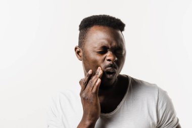 Afrikalı Amerikalı adam yanağına dokunuyor ve diş ağrısı ve diş rahatsızlığı çekiyor. Diş çürüğü, enfeksiyon ya da diş eti yaralanması olan Afrikalı bir adam.